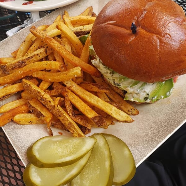 A Gold Standard Cafe burger with fries and pickles on a white plate.