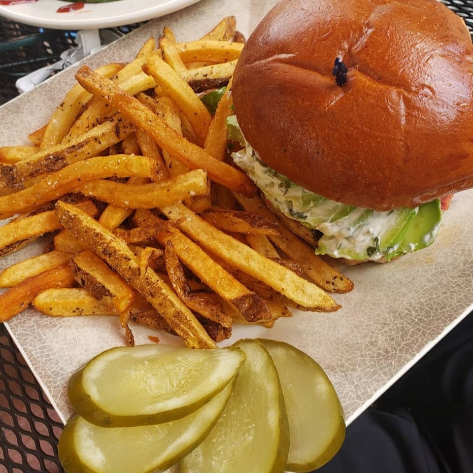 A Gold Standard Cafe burger with fries and pickles on a white plate.