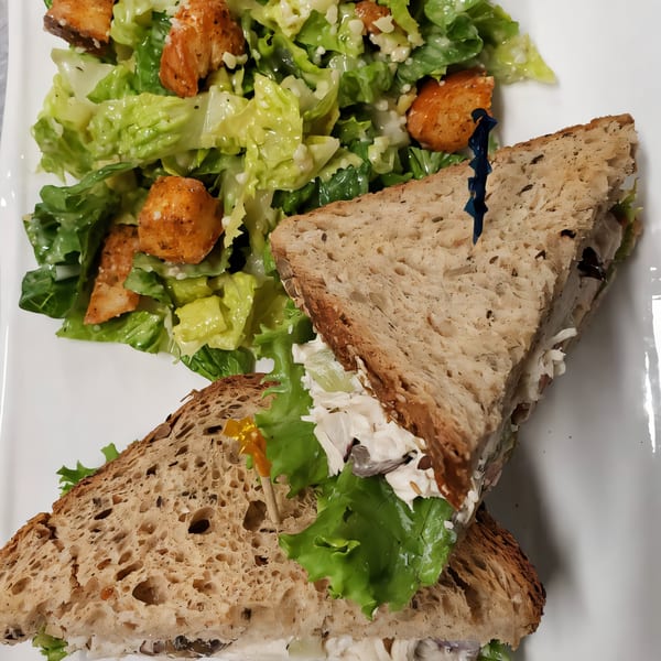 A Gold Standard Cafe chicken salad sandwich on whole wheat bread with a side Caesar salad.