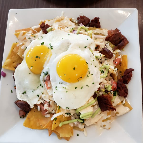 Chilaquiles with two fried eggs, cheese, avocado crema, and chorizo on a white plate.