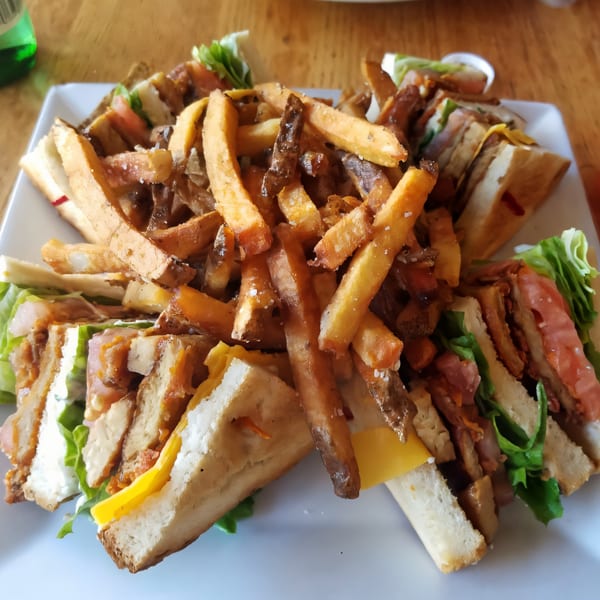 A large plate of Gold Standard Cafe's club sandwiches cut into triangles, piled high with seasoned fries.