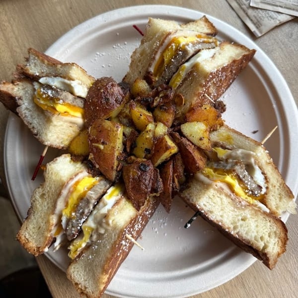 Four French toast breakfast sandwiches with sausage, egg, and cheese, served with home fries.