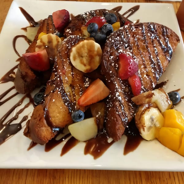 Golden French toast drizzled with chocolate sauce, powdered sugar, and topped with fresh fruit.